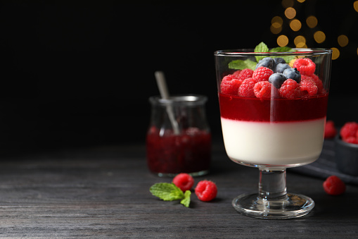Delicious panna cotta with berries on black wooden table. Space for text