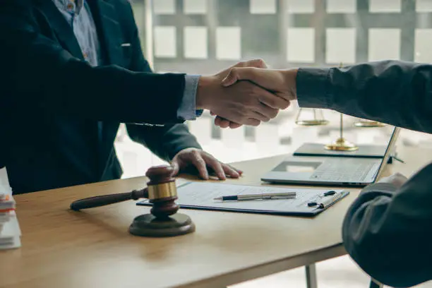 Businessmen shake hands to make deals with male lawyers, judges, legal advisors. Contract consulting services to plan a court case Businessmen and lawyers discuss contract documents at the table.