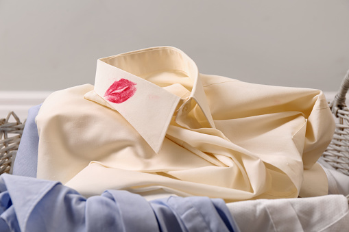 Men's shirt with lipstick kiss marks among other clothes in laundry basket indoors, closeup