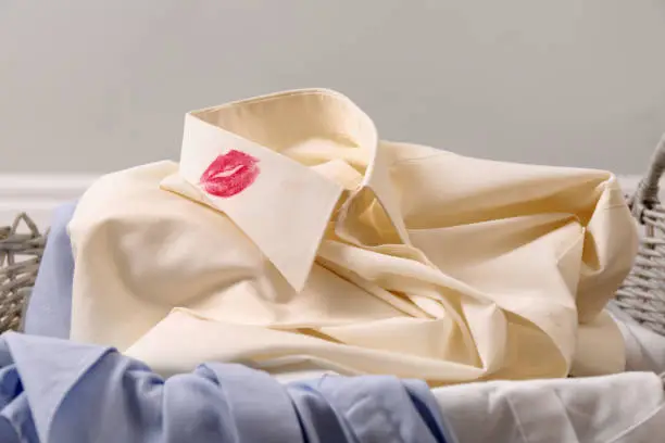 Men's shirt with lipstick kiss marks among other clothes in laundry basket indoors, closeup