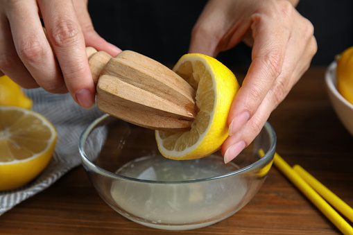 Woman squeezing lemon juice with citrus reamer at wooden table, closeup