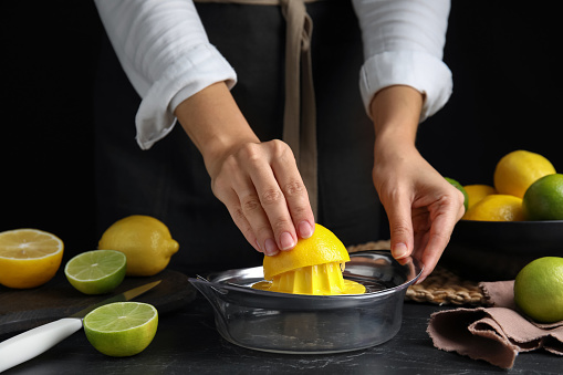 Woman squeezing lemon juice at black table, closeup