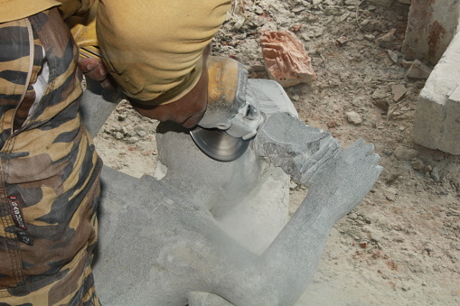 Close-up of Indian craftsman carving traditional Hindu God and Goddess stone Sculpture or statue, using Industrial Equipment, hand moving, Bhadrak, Odisha, India