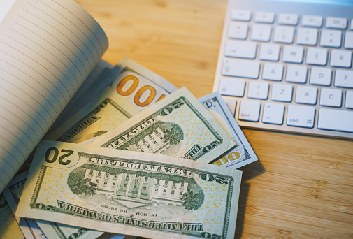 US Dollars copybook next to computer keyboard on the wooden table