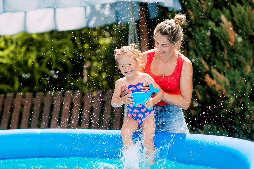 Mom and daughter have fun in the pool in the garden, dipping into the warm water.