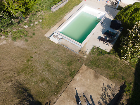 Drone flight over pool in the middle of greenery, fresh grass grown and the pool is not yet cleaned