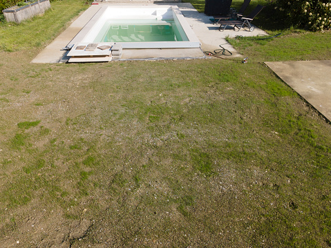 Drone flight over pool in the middle of greenery, fresh grass grown and the pool is not yet cleaned