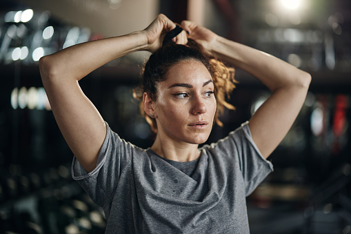 Young female athlete tying hair before sports training in a gym.