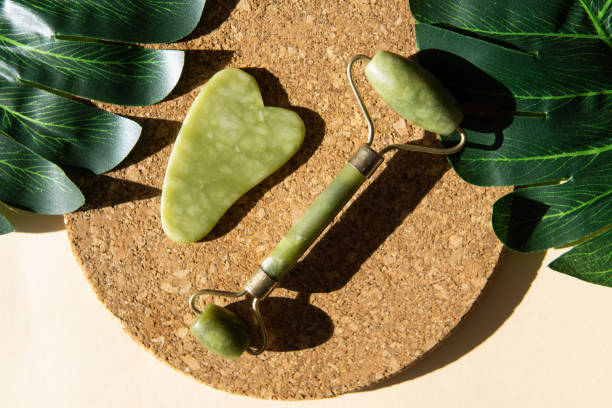 istock Jade Gua sha scraper and face roller massager on a cork round stand with a monstera leaf. 1397697670