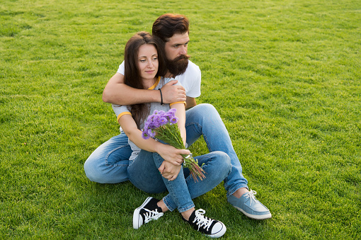 During outdoor recreational activities. Couple in love sit on green grass outdoor. Summer vacation. Enjoying fresh outdoor air. Rest and relaxation. Healthy outdoor recreation. Summertime.