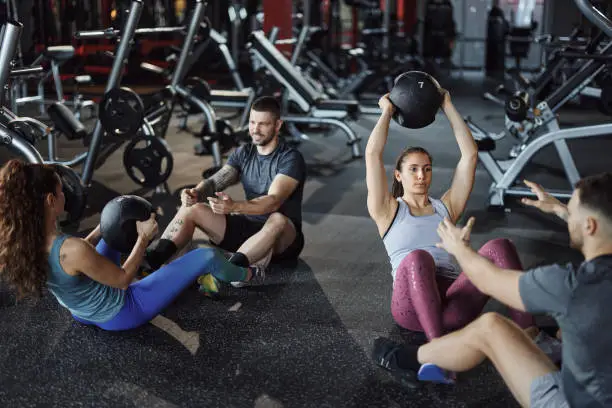 Athletic couples cooperating while exercising sit-ups with medicine ball during sports training in a gym.