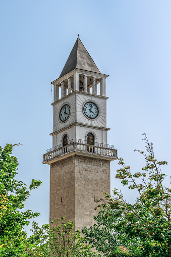 Clock Tower of Tirana against the blue sky in Albania. Square chapel in Islamic style among greenery, close-up