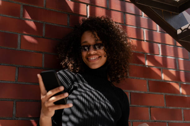 istock Woman smiling and using smart phone near brick wall 1397700230