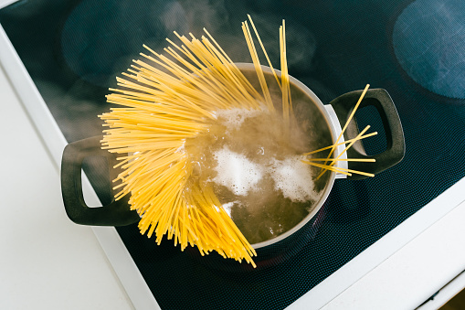 Spaghetti in pot is cooked in boiling water on electric ceramic hob. Top view, soft focus, yellow gluten free corn pasta cooking bolognese