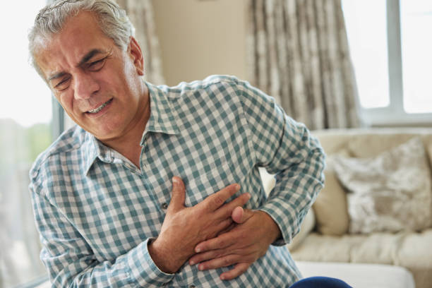 mature man clutching chest and suffering heart attack at home - kalp krizi stok fotoğraflar ve resimler