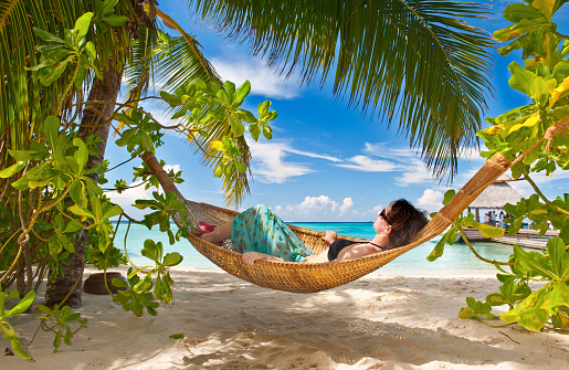 Girl is sleeping in the hammock under the palms on the tropical Maldivian beach