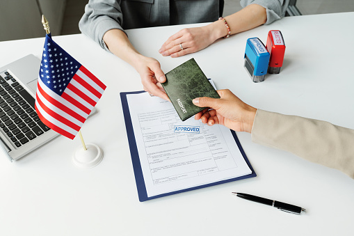 High angle of unrecognizable woman giving her passport to consular officer to make USA travel visa after application approval