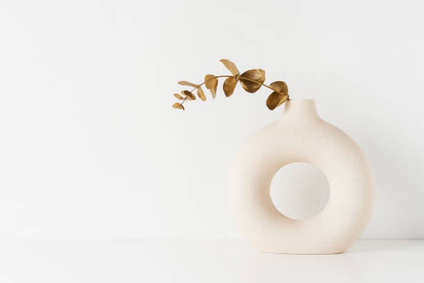 istock Round vase with a golden-colored eucalyptus branch on a white table by the wall. 1397708931