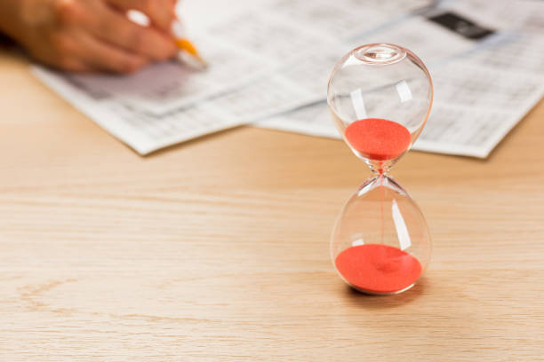 istock Hourglass with time running out and student hand testing in exercise and passing exam carbon paper computer sheet with pencil in school test room 1397710230