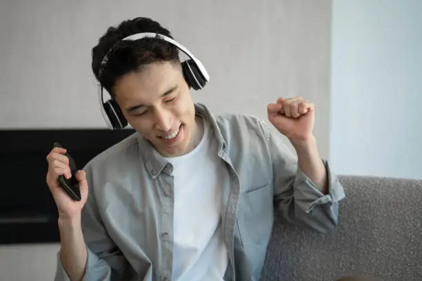 Photo of Cheerful Asian man listens favorite music moving in rhythm