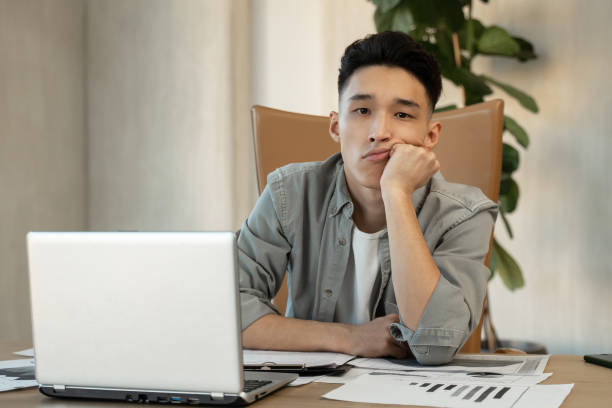 istock Tired Asian man sits in office propping up head with hand 1397710401