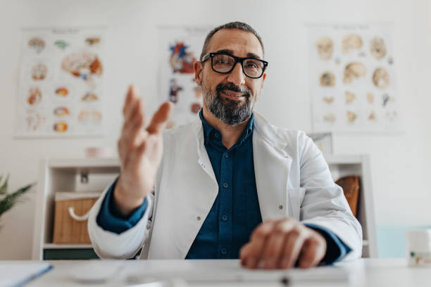 Let me explain Mid adult doctor sitting and wearing lab coat talking using video call with the patients doctor head stock pictures, royalty-free photos & images