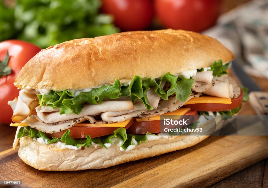 Turkey and ham submarine sandwich Submarine sandwich made with turkey, ham, cheese lettuce and tomato on a hoagie roll with lettuce and tomatoes in background Submarine Sandwich Stock Photo
