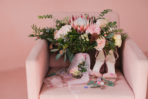 Ramo con cintas de seda, zapatos clásicos femeninos, anillos de boda y anillo de compromiso en una silla vintage rosa. photo