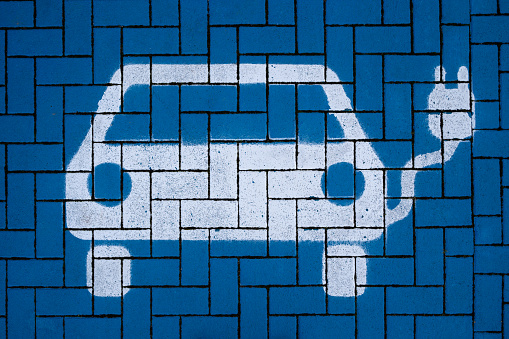 White electric vehicle symbol on blue paving stones in a charging station