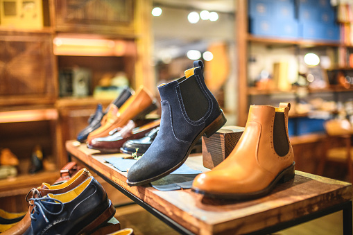 Close-up shot of blue and caramel color leather boots and shoes for men on wooden shelves. The footwear is handmade with high quality materials by professional shoemakers.