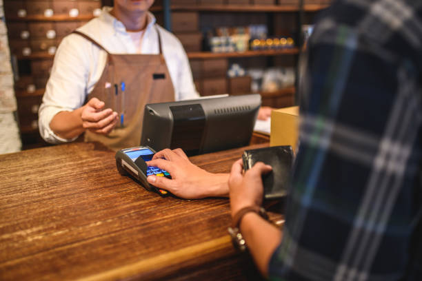 Male Adult Customer Buying With A Credit Card In A Menswear Clothing Store Male adult client purchasing clothes and shoes with a credit card at a menswear department store. He is holding his wallet with one hand and with the other he is inserting the PIN number in the card reader. shoe store stock pictures, royalty-free photos & images