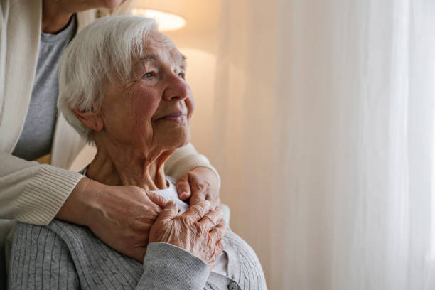 Portrait of elderly woman. Unrecognizable female expressing care towards an elderly lady, hugging her from behind holding hands. Two adult women of different age. Family values concept. lose up, copy space, background. adult offspring stock pictures, royalty-free photos & images