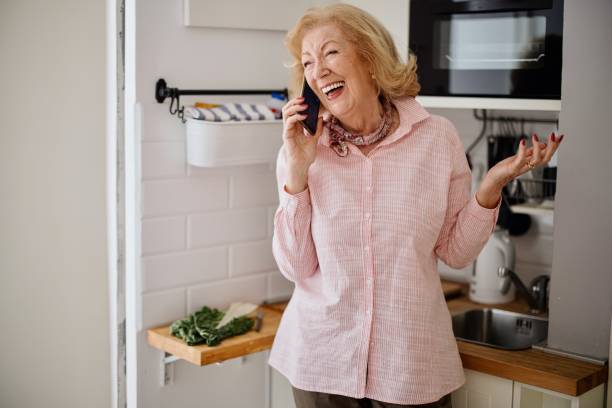 istock Smiling senior woman using her phone in the kitchen 1397727781