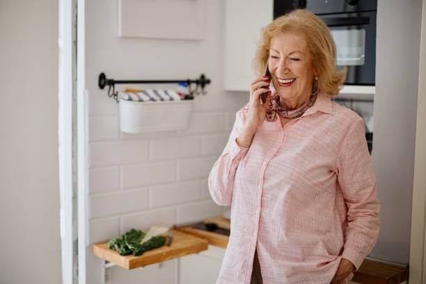 istock Smiling senior woman using her phone in the kitchen 1397727783
