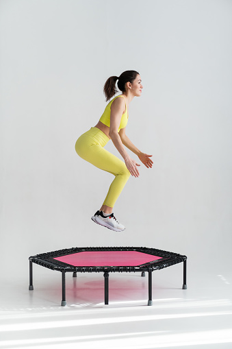 young fitness woman In sportswear jumping on sport trampoline White background