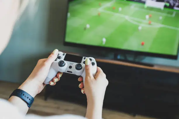 Photo of Girl playing a video game console. Game is football. Joystick in hands. Selective focus