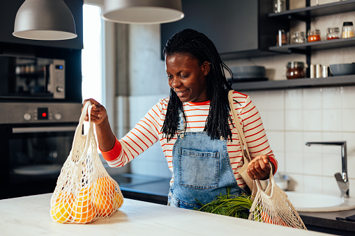 An african american woman is putting her fresh produce groceries onto the counter top in the kitchen