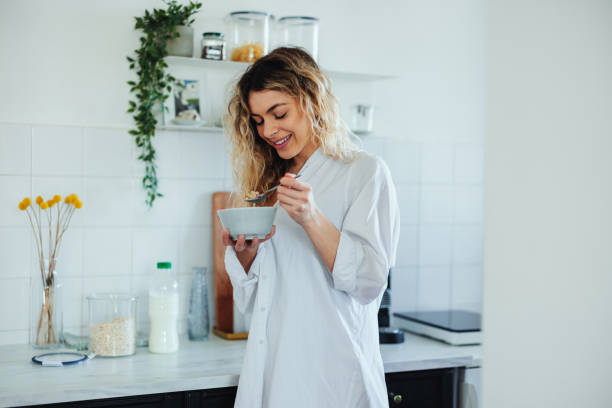 donna a casa che mangia una ciotola di cereali per colazione - eating women breakfast cereal foto e immagini stock