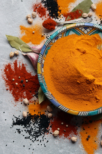 Decorative blue plate full of turmeric powder. Close up photo of aromatic spices. Silver spoon with paprika powder. Light grey background. Healthy eating concept.