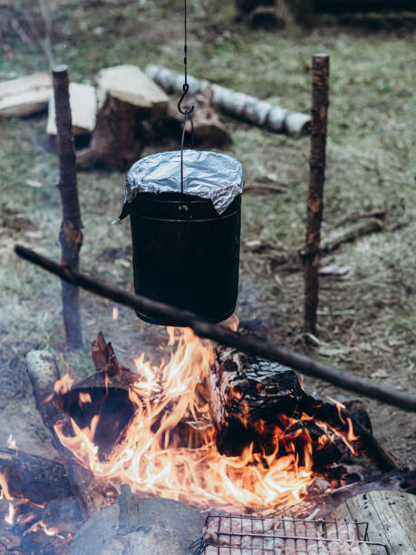 The kettle hangs over the fire. Cooking at the campsite. The kettle hangs over the fire. Cooking at the campsite. Camping detail, travel lifestyle photo. survival tools stock pictures, royalty-free photos & images
