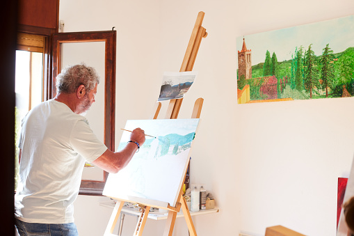 A senior man paints in a small apartment room.