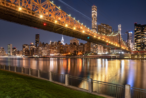 Illuminated Queensborough Bridge spanning from the Upper East Side of Manhattan to Roosevelt Island. Evening view of New York City skyscrapers across the East River. USA