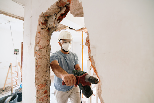 Construction worker wearing all safety measures demolishing a brick wall inside a house