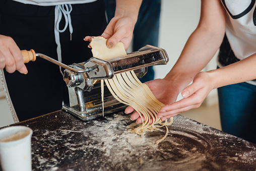 Homemade italian pasta preparation with paste machine. Close-up of two girls hands cooking traditional italian pasta