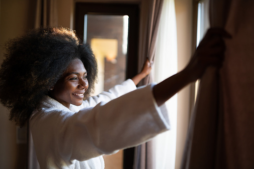 African woman pulling curtains in hotel room