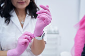 Close up photo of woman cosmetologist putting on pink sterile gloves