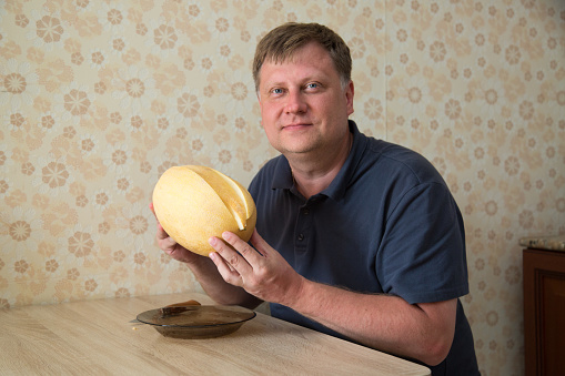 An adult man is blond with a large yellow fragrant melon waiting for lunch.