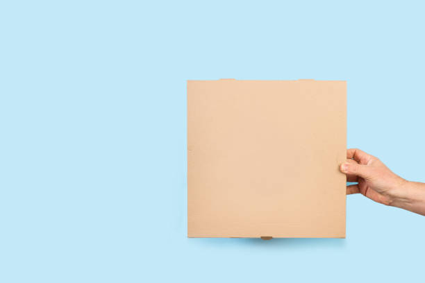istock Man hand holding a brown pizza box on a light blue background 1397745555
