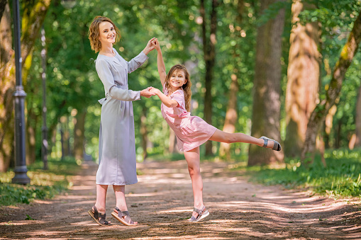 Mother and daughter are playing dancing in the park. Happy family concept. Beauty nature scene with family outdoor lifestyle. Happy family resting together. Happiness and harmony in family life.