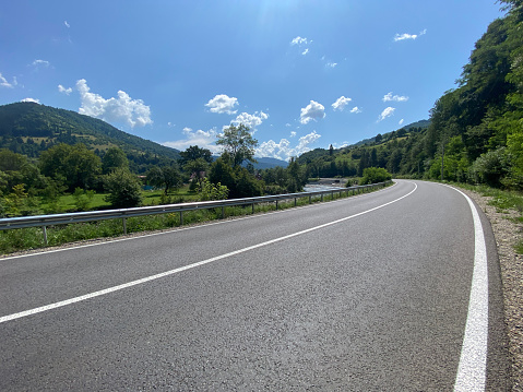 Empty country road and green mountains in summer. Cloudy blue sky. Solid road markings